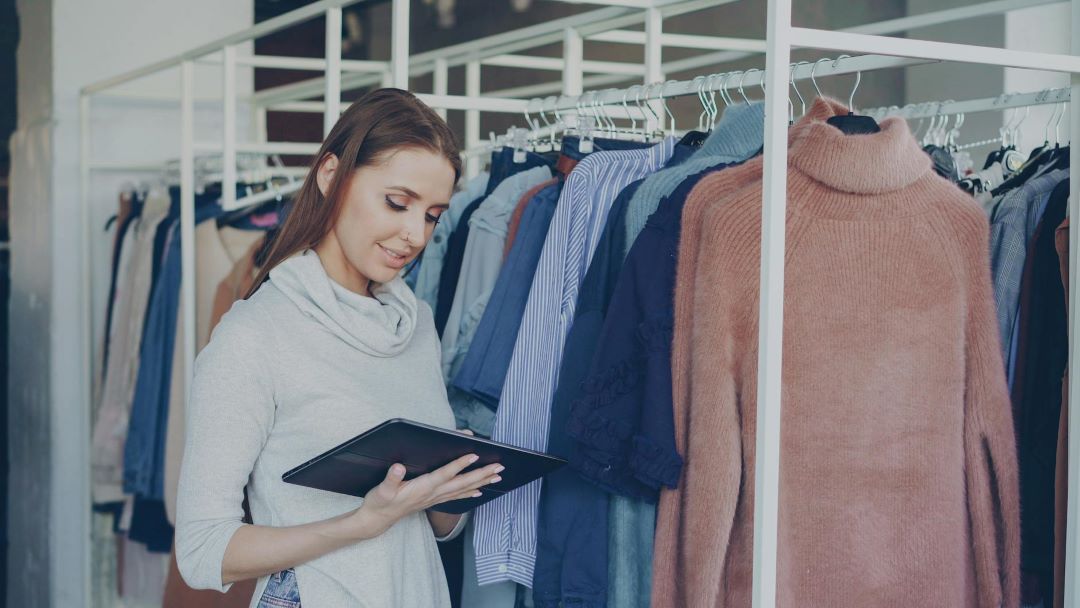 Adiós al caos del inventario: cómo un programa de gestión para tiendas unifica tus ventas físicas y online Mujer con tablet y ropas